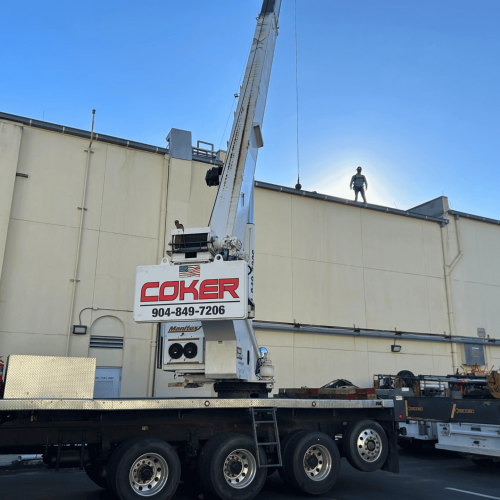A Coker crane in front of a building with a man standing on the roof.